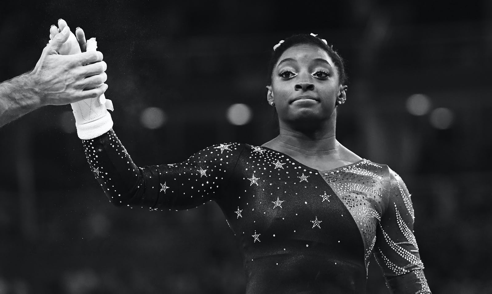 A black and white photo of Simone Biles high diving someone out of frame.