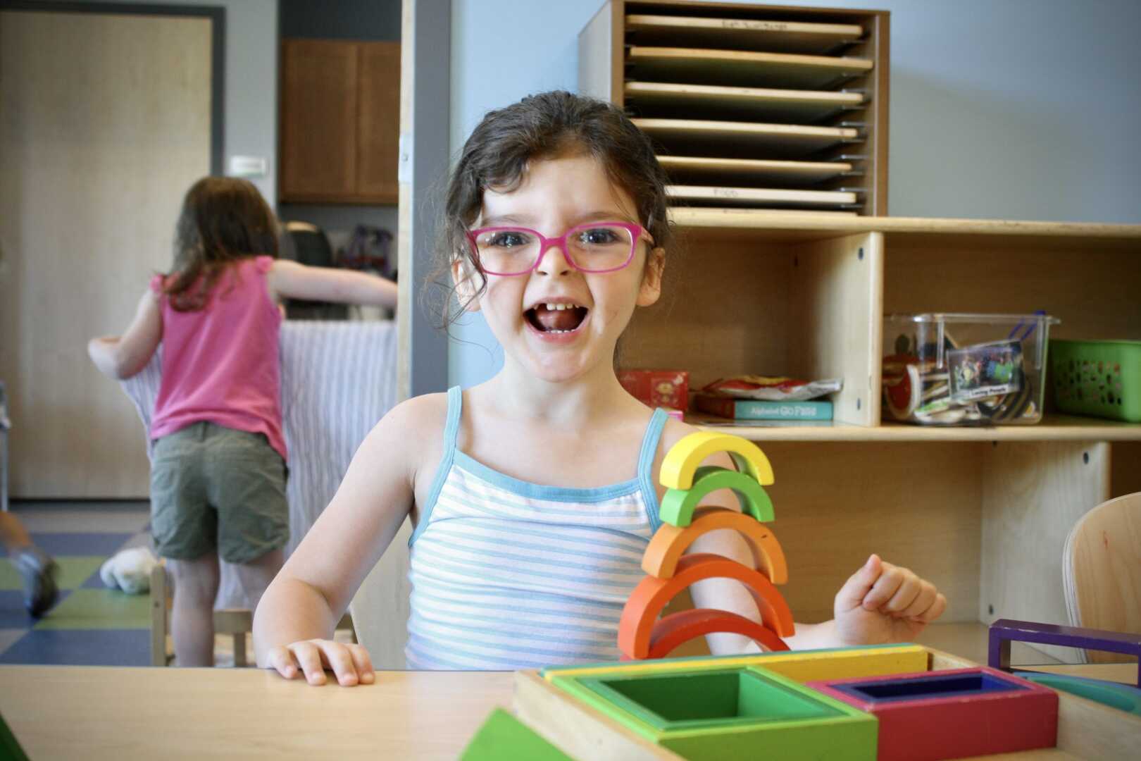 A young girl smilies after stacking arched colorful blocks on top of each other.