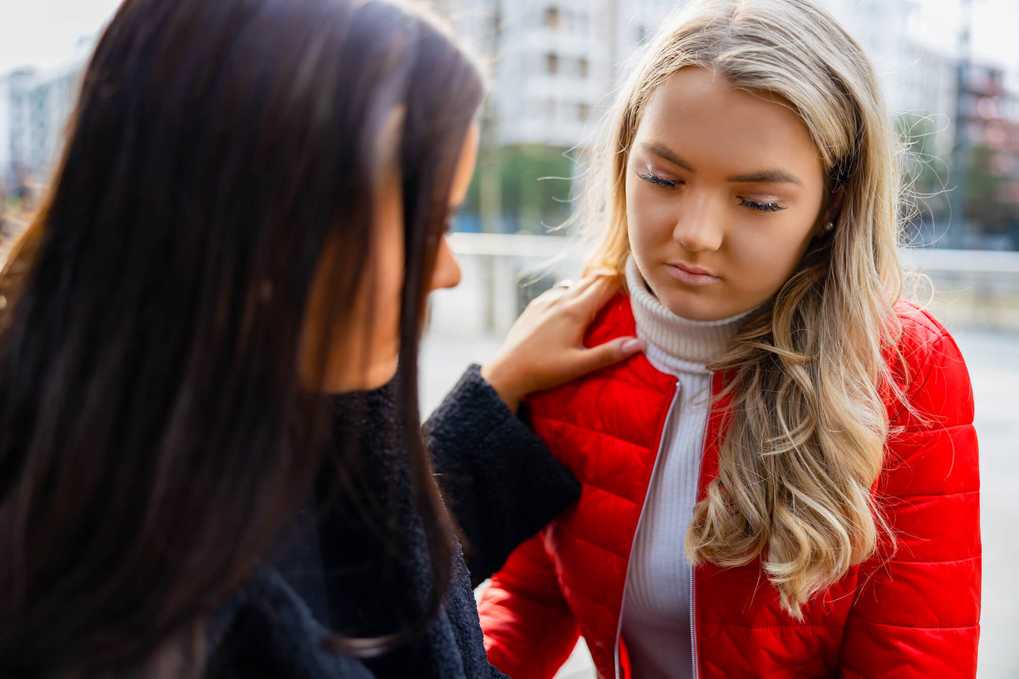 A woman consoles a young girl in a red coat and white turtle neck.