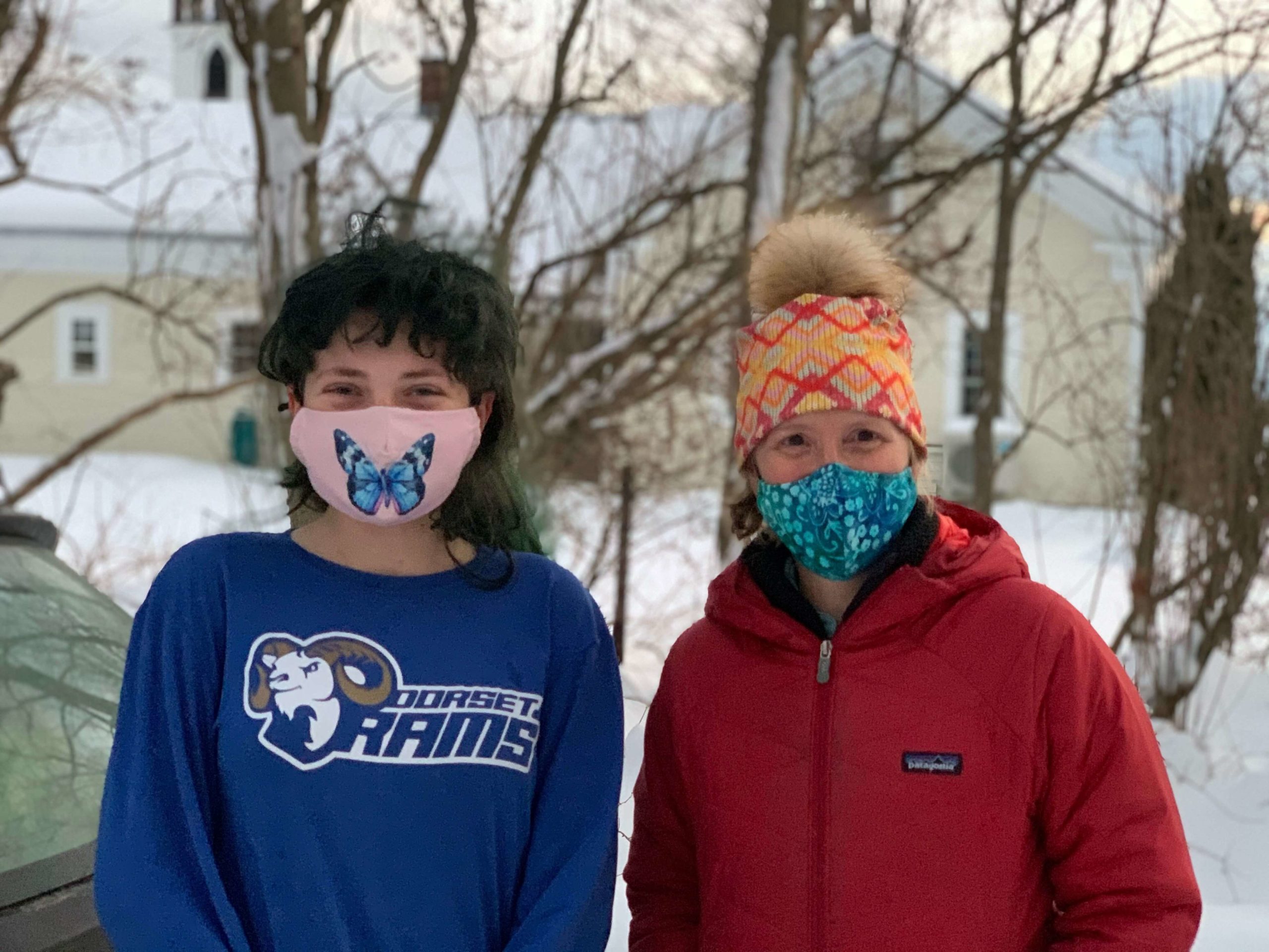 Two masked women wearing coats smiling at the camera outside in winter