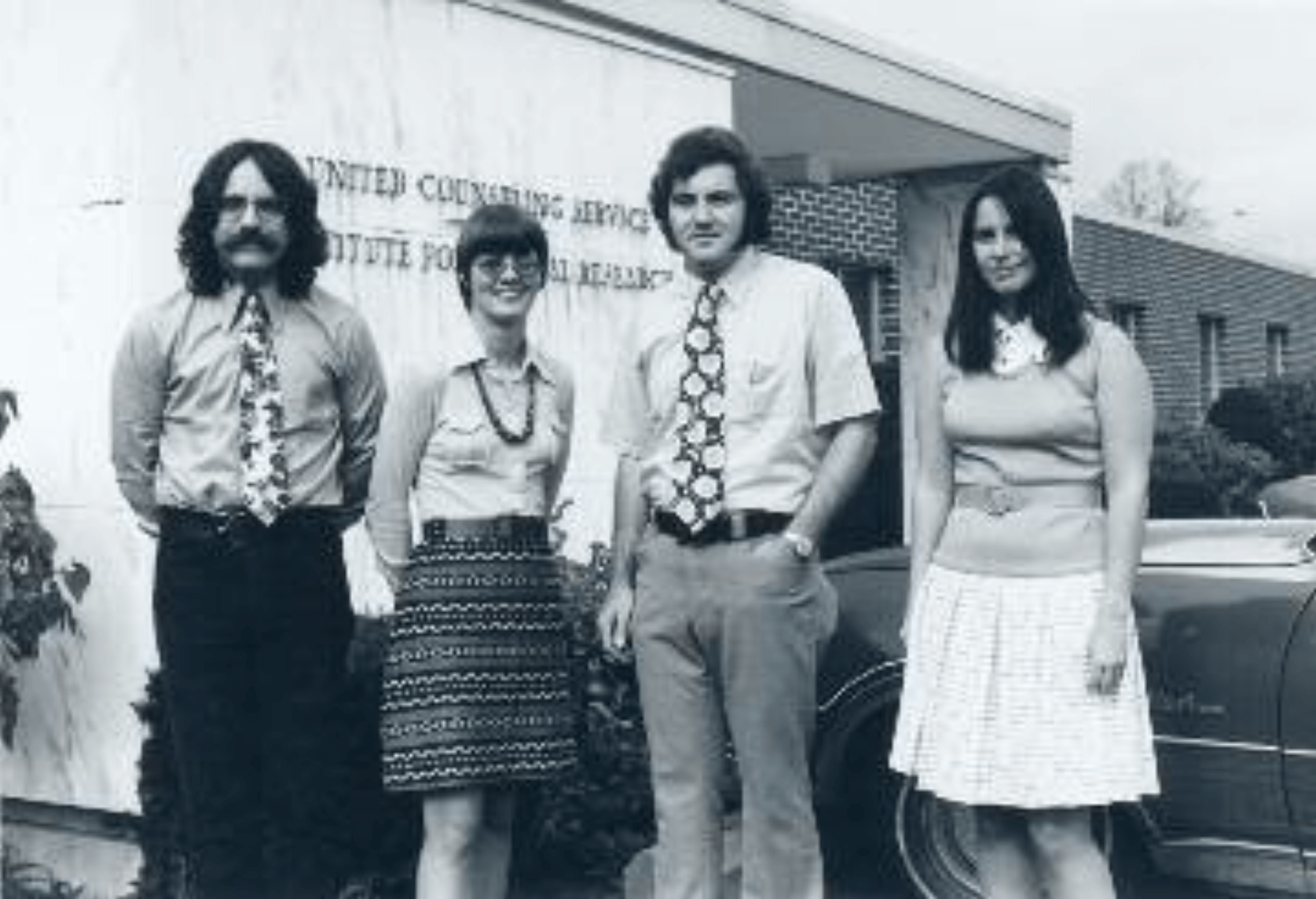 A black and white photo of two men and two women in front of an old United Counseling Service sign. This appears to be taken in the 1960s or 70s