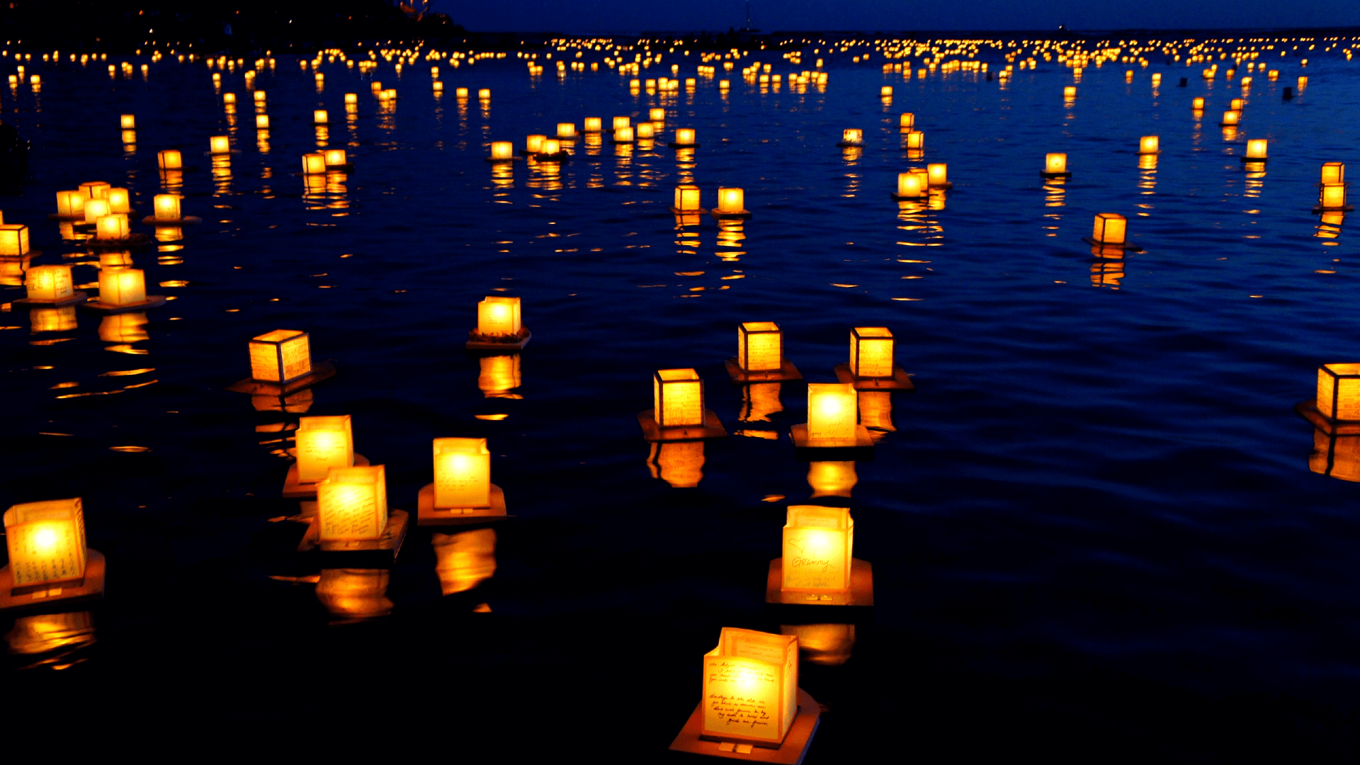 Hundreds of glowing paper lanterns floating on a lake in the night.