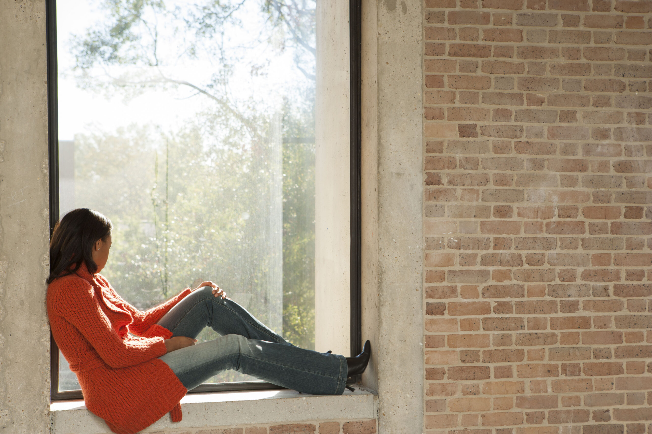 College student in classroom sitting on window sill.