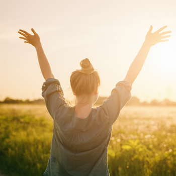 Women stretching her arms up towards the sunshine in an open field.