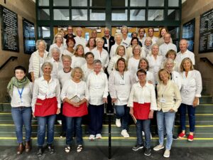 A group of women wearing white button down shirts and some wearing red half aprons post for a group photo.