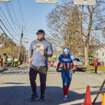An adult in a t-shirt and child wearing a Captain America costume run on the road.