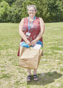 A person wearing a coral colored floral sleeveless dress smiles for a photo while holding a gift bag.