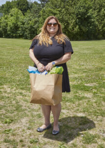 A person wearing a black short sleeved dress holds a gift bag and smiles for a photo.
