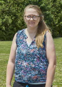 A person wearing a blue sleeveless blouse and glasses poses for a photo.