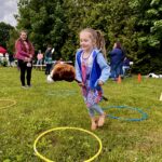 A young child with blonde pigtails smiles while playing with a horse toy and hula hoops.