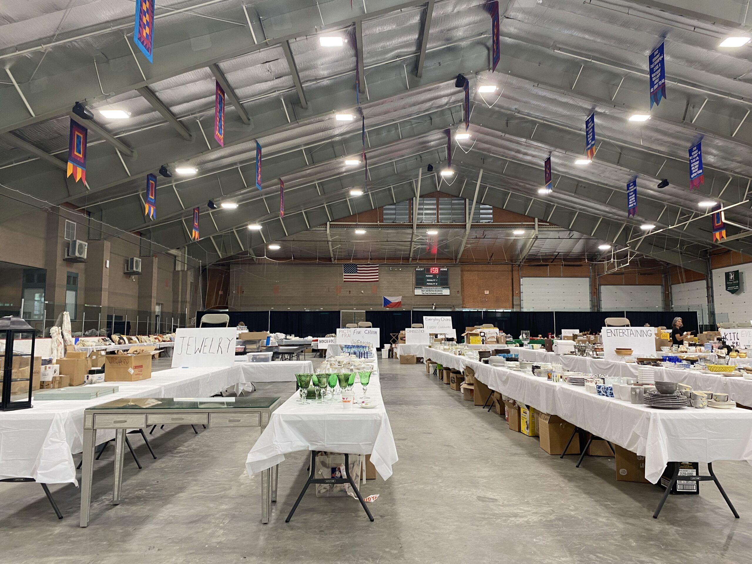 Rows of long tables with white tablecloths holding antiques and other wares fill a large gymnasium.