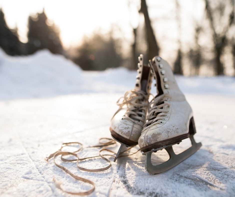 A pair of scuffed ice skates rests on an ice rink with a light dusting of snow on top.