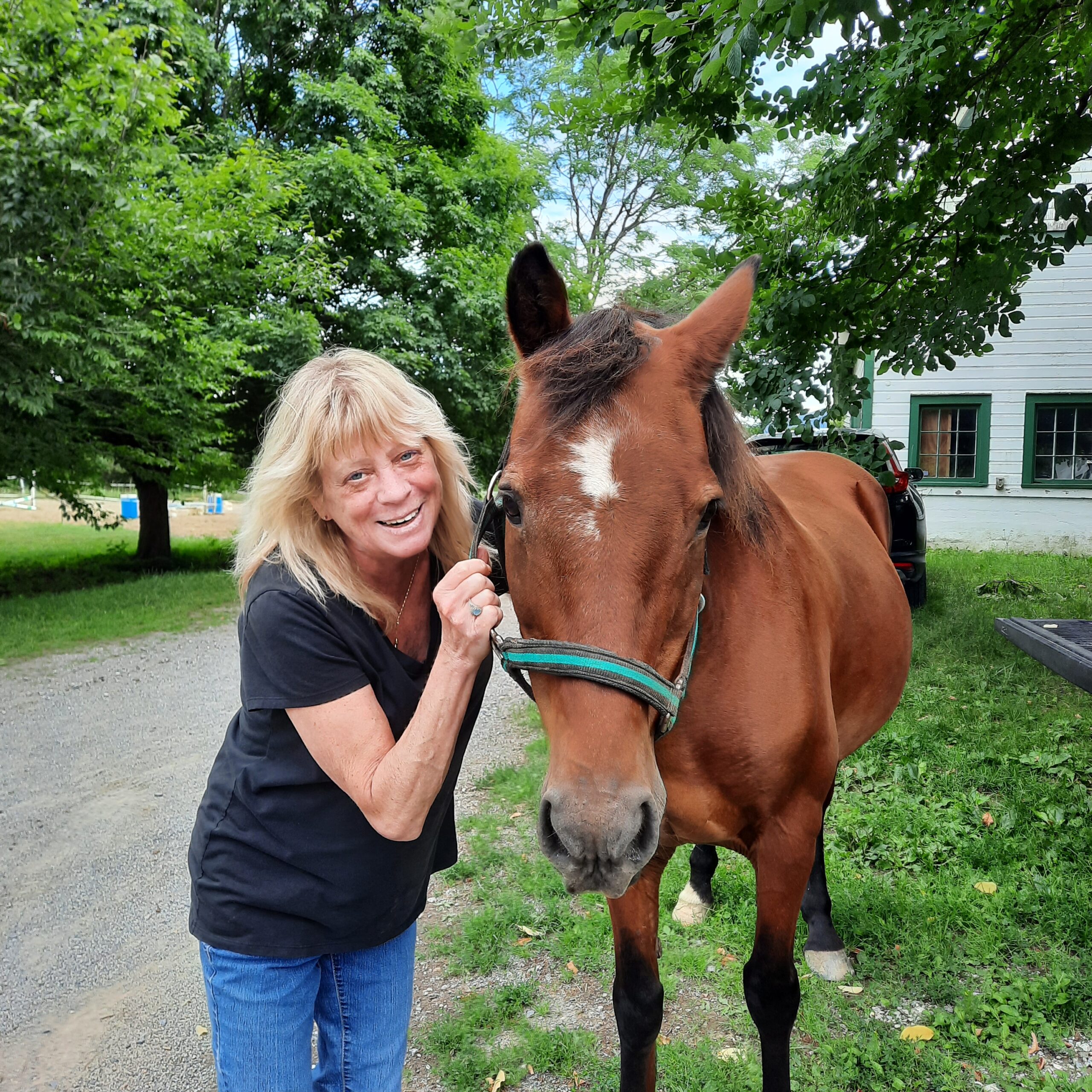 Woman in black shirt smiling and holding the reigns of a brown horse.