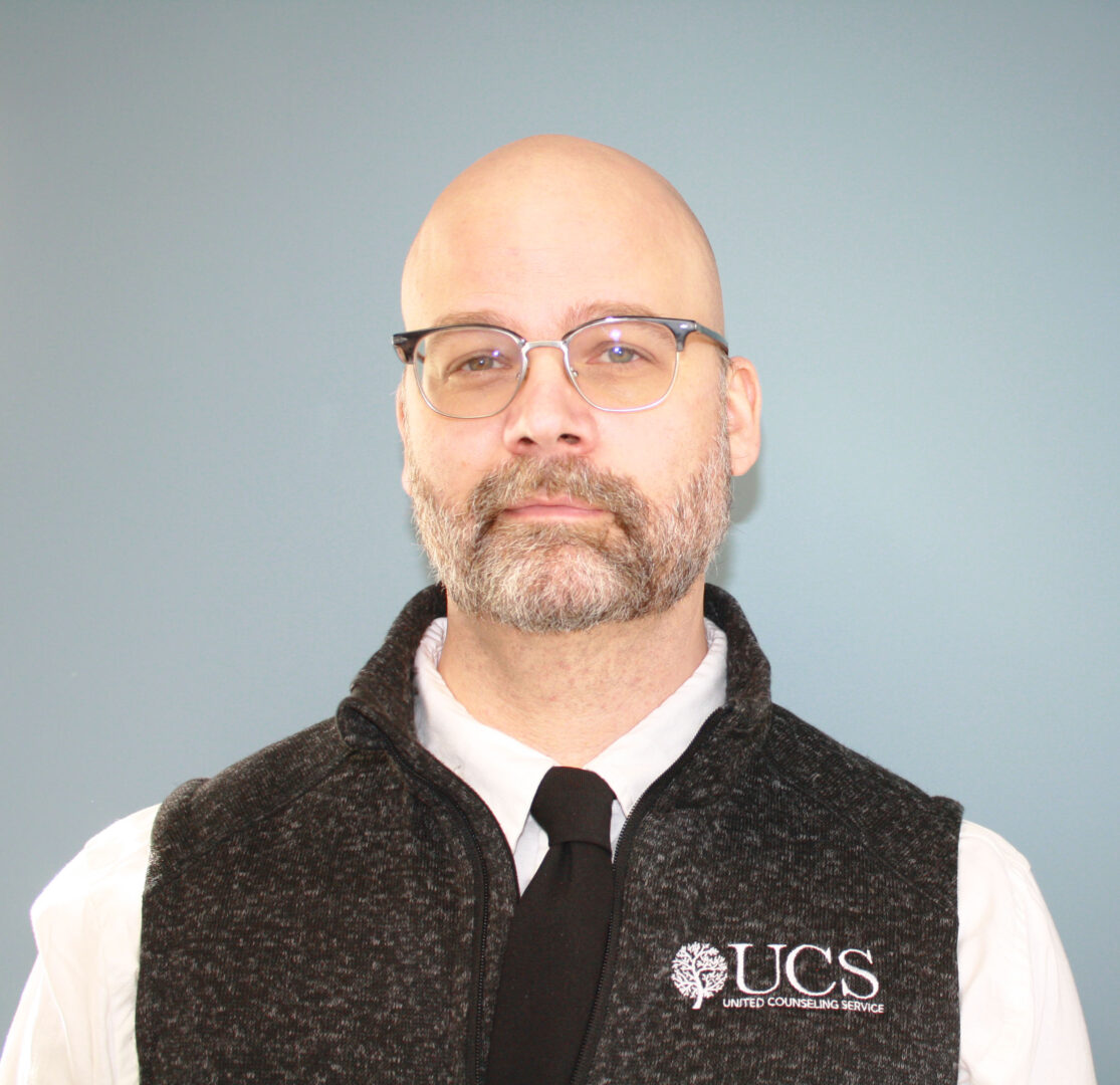 A man with glasses and wearing a black vest with UCS logo, and tie
