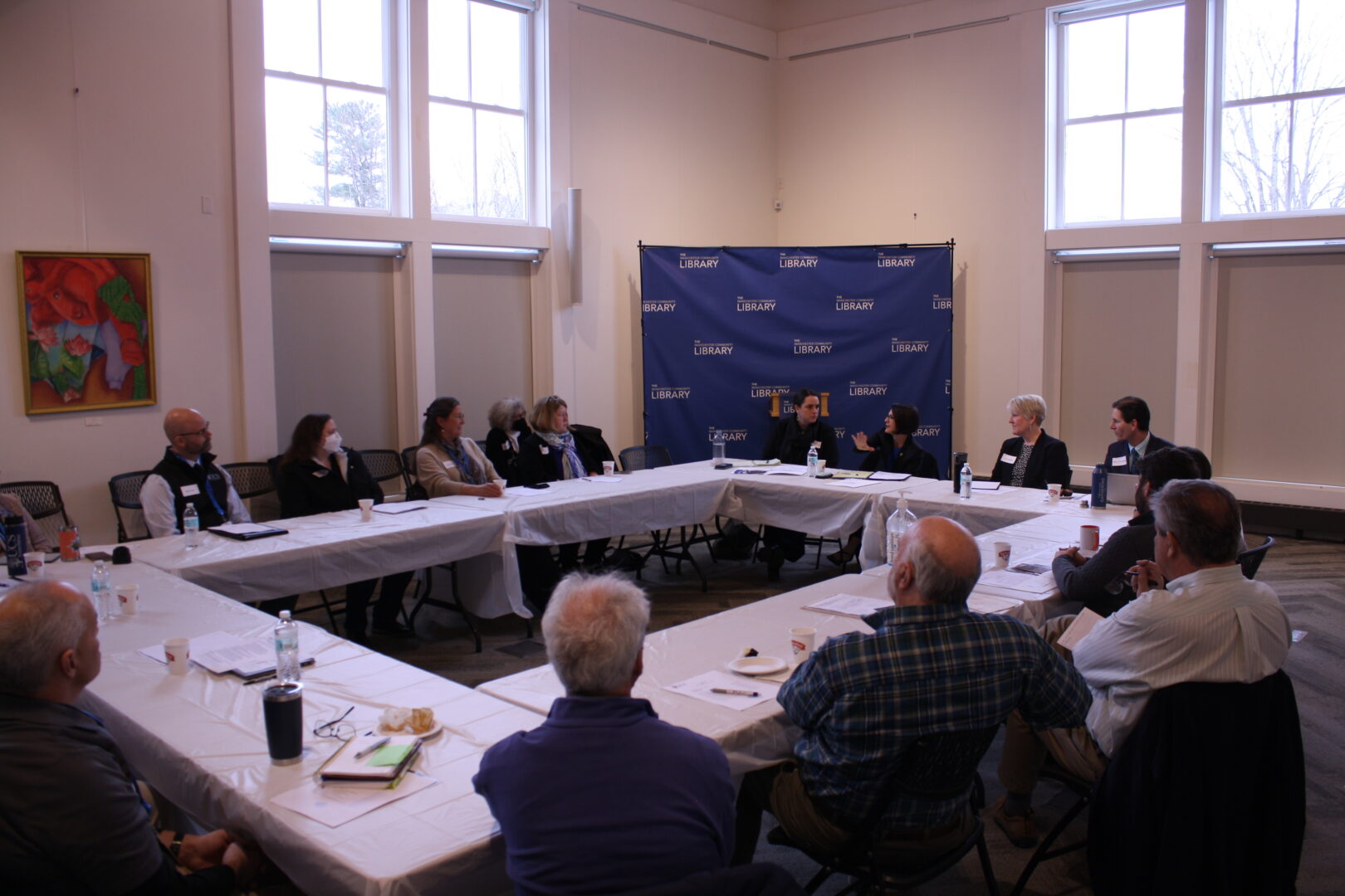 A group of adults speaks with each other while sitting at tables arranged in a large rectangle.