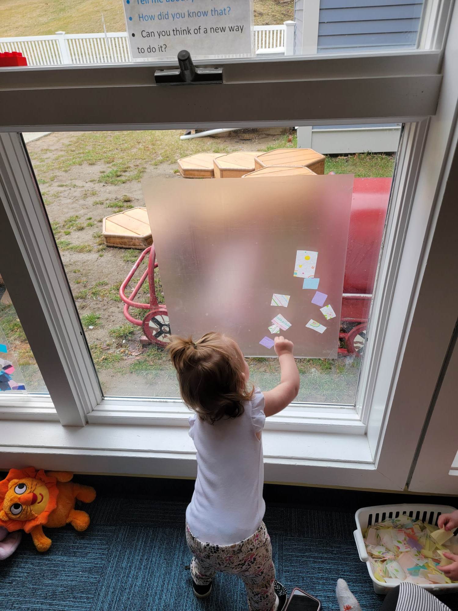 A young child with a ponytail puts art on a window.