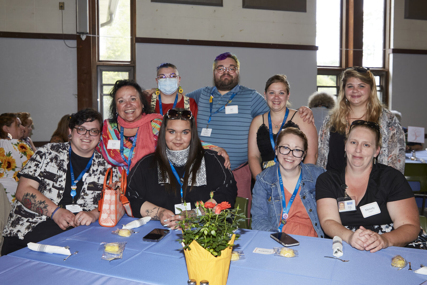 Several staff members sit together at a table with a light blue tablecloth and a small pot of pink roses in a yellow wrapper.