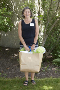 Middle-aged women with short brown hair, standing while holding a big bag smiling