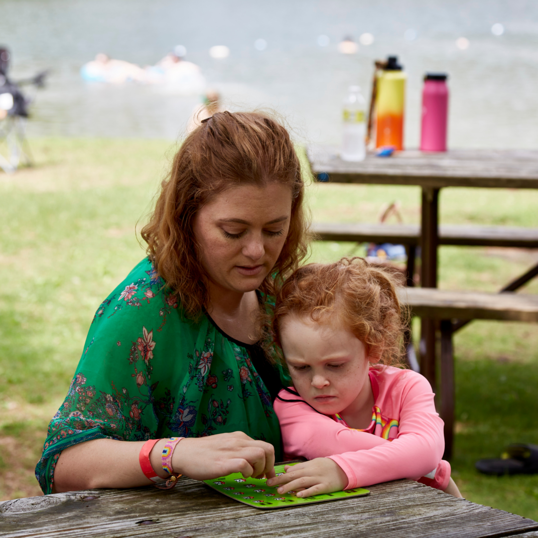 a mother and daughter sitting together outside looking at a game together