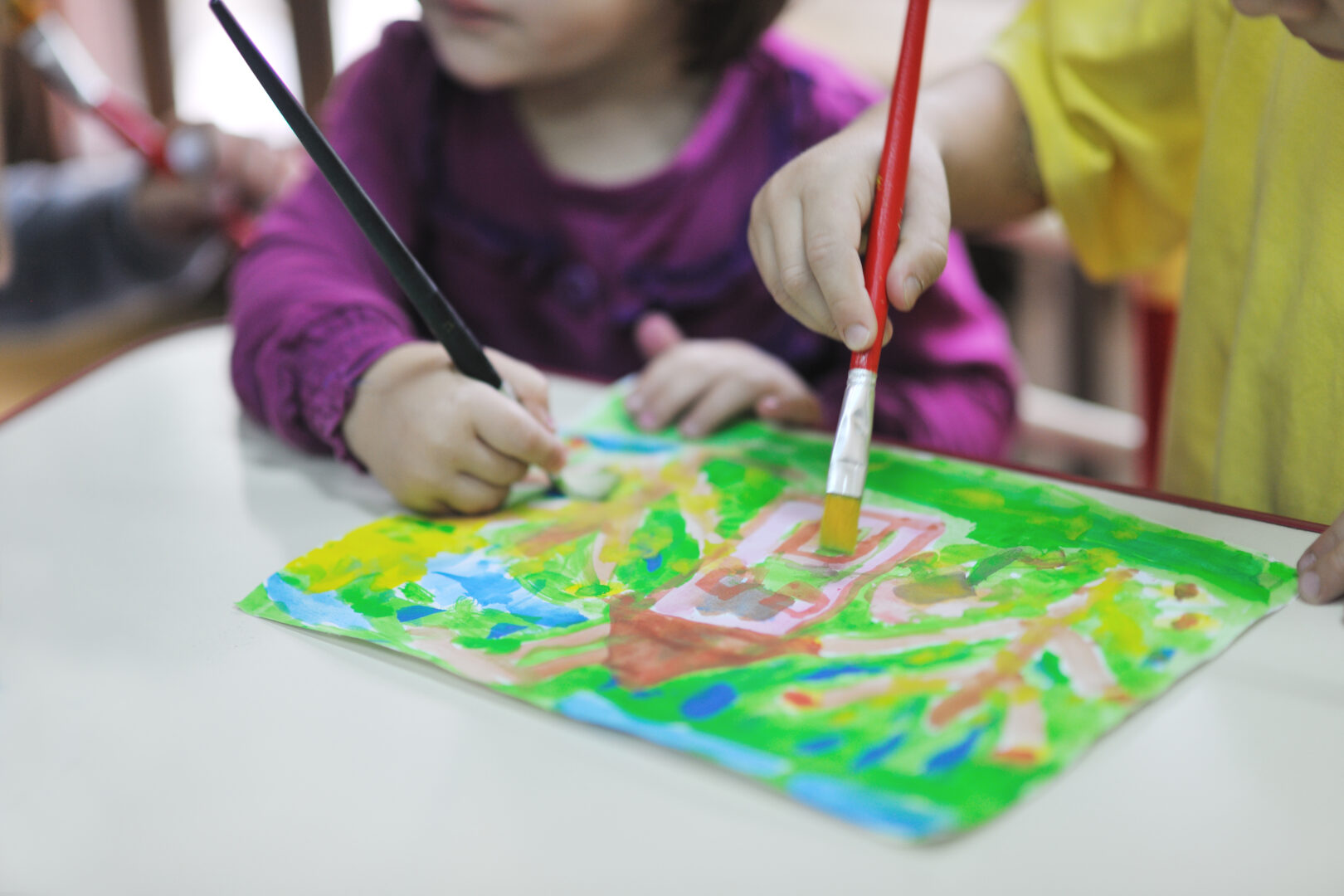Close up of two young children painting a picture of a house against a green landscape
