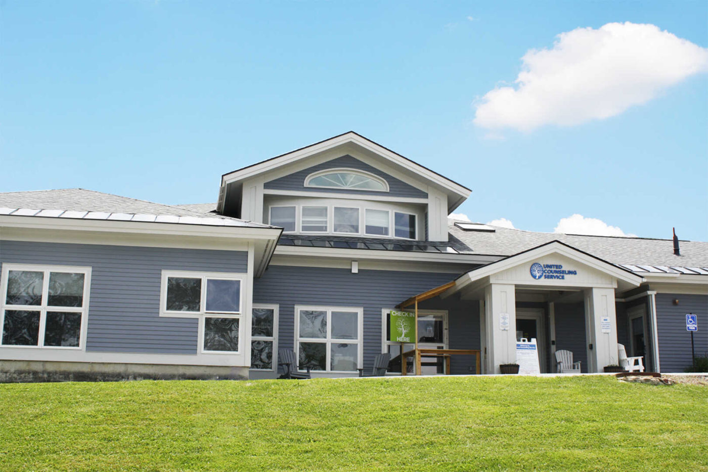 large light blue/grey building set against a blue sky with a puffy white cloud and green grass in the foreground