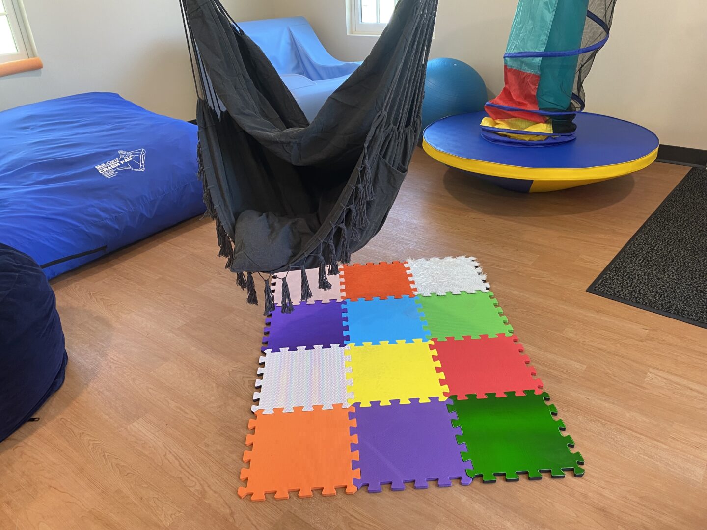 room with colorful activities like a cloth swing, rainbow puzzle piece floor pad, and balance board