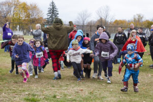 kids run towards the camera in an outdoor race setting while wearing superhero costumes