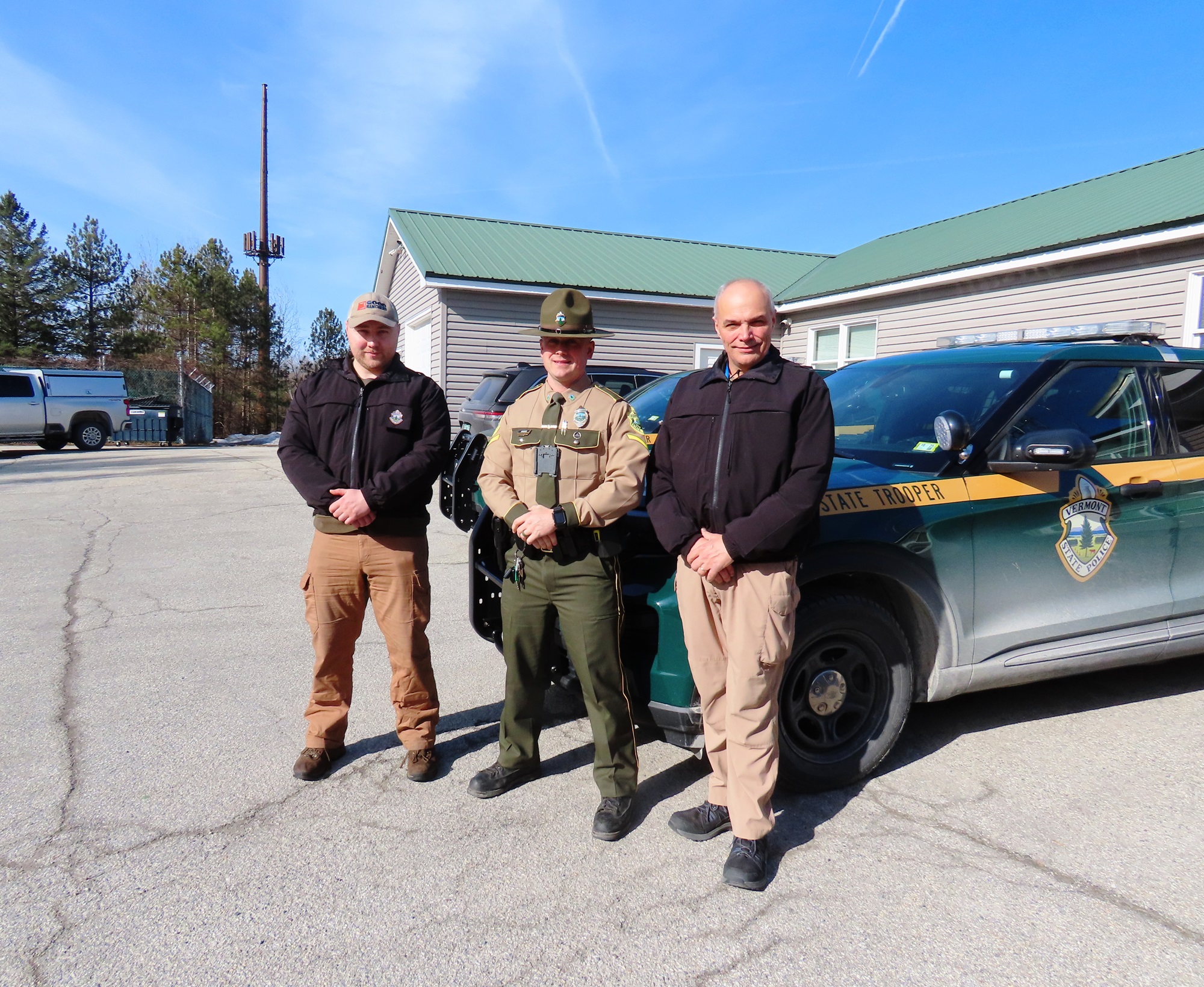 Two men stand on either side of a state trooper.
