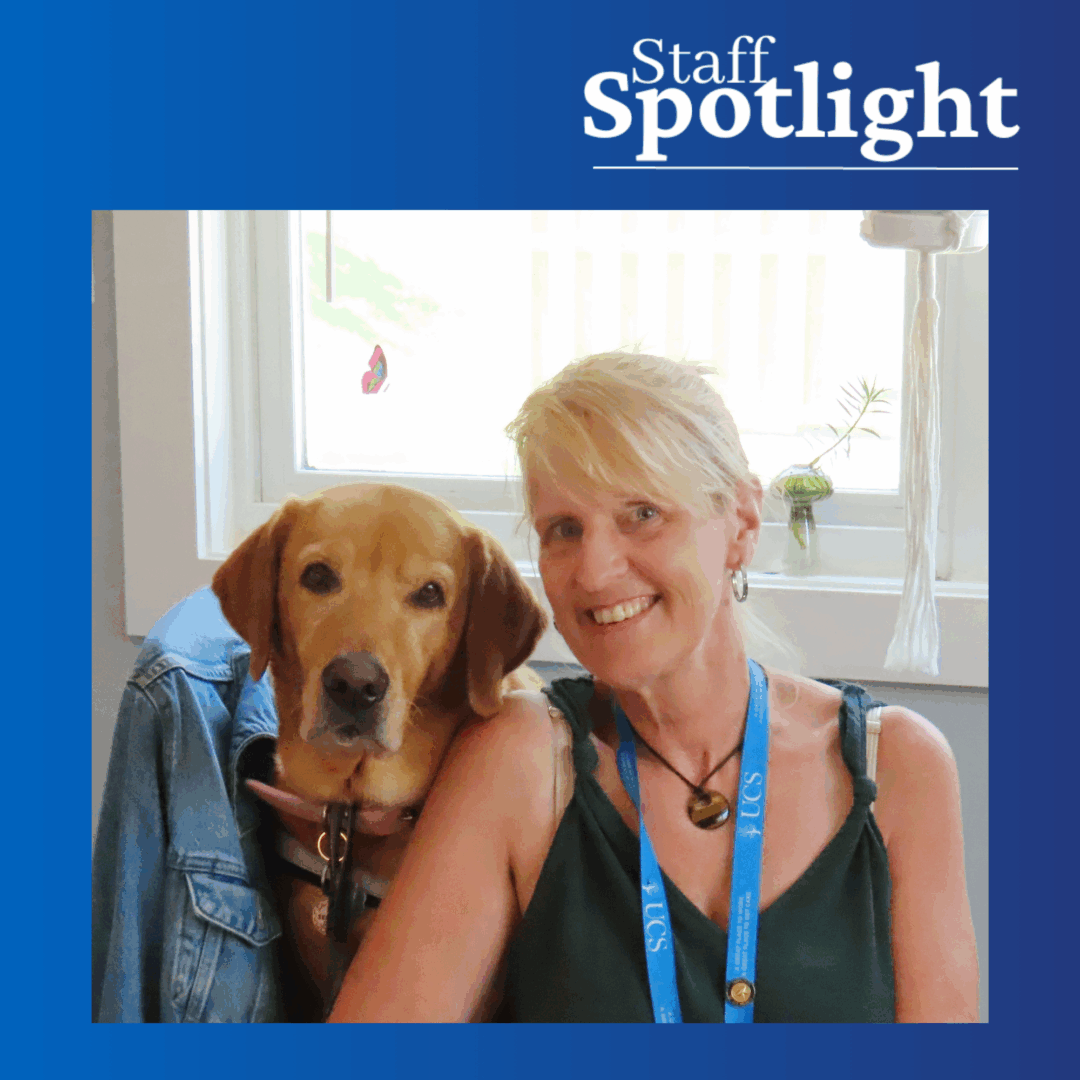A blonde woman wearing a green tank top and blue lanyard and necklace sits next to a large light brown dog (lab or lab mix). There is a blue gradient background behind the photo and Staff Spotlight in white text on the top right.