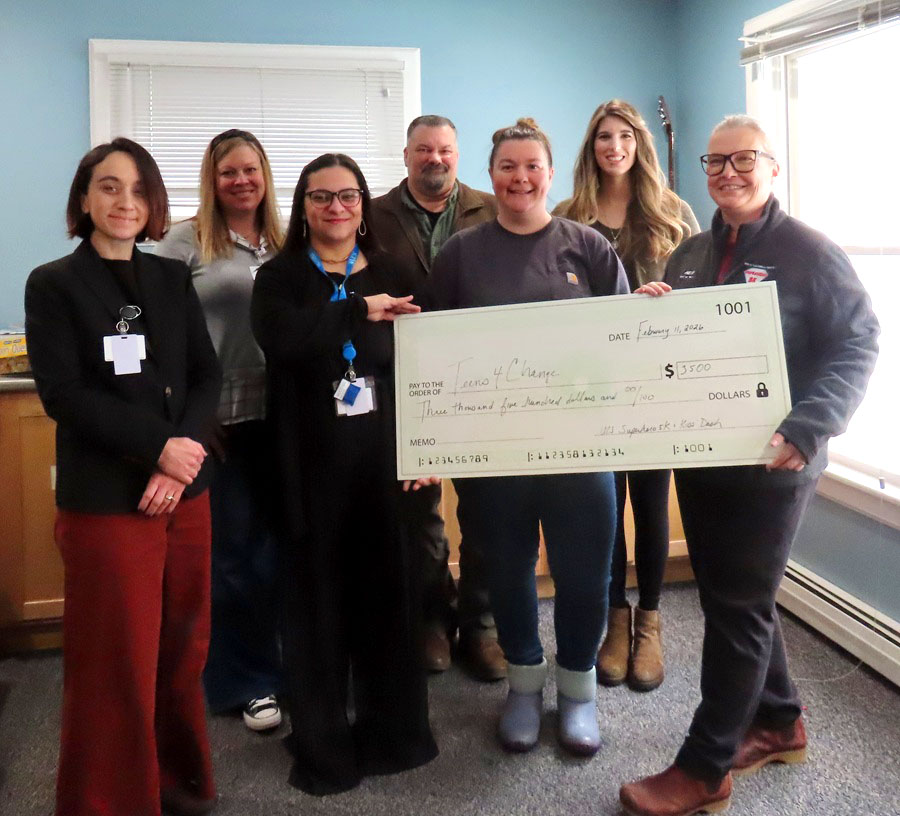 A group of seven people smile while presenting a large check