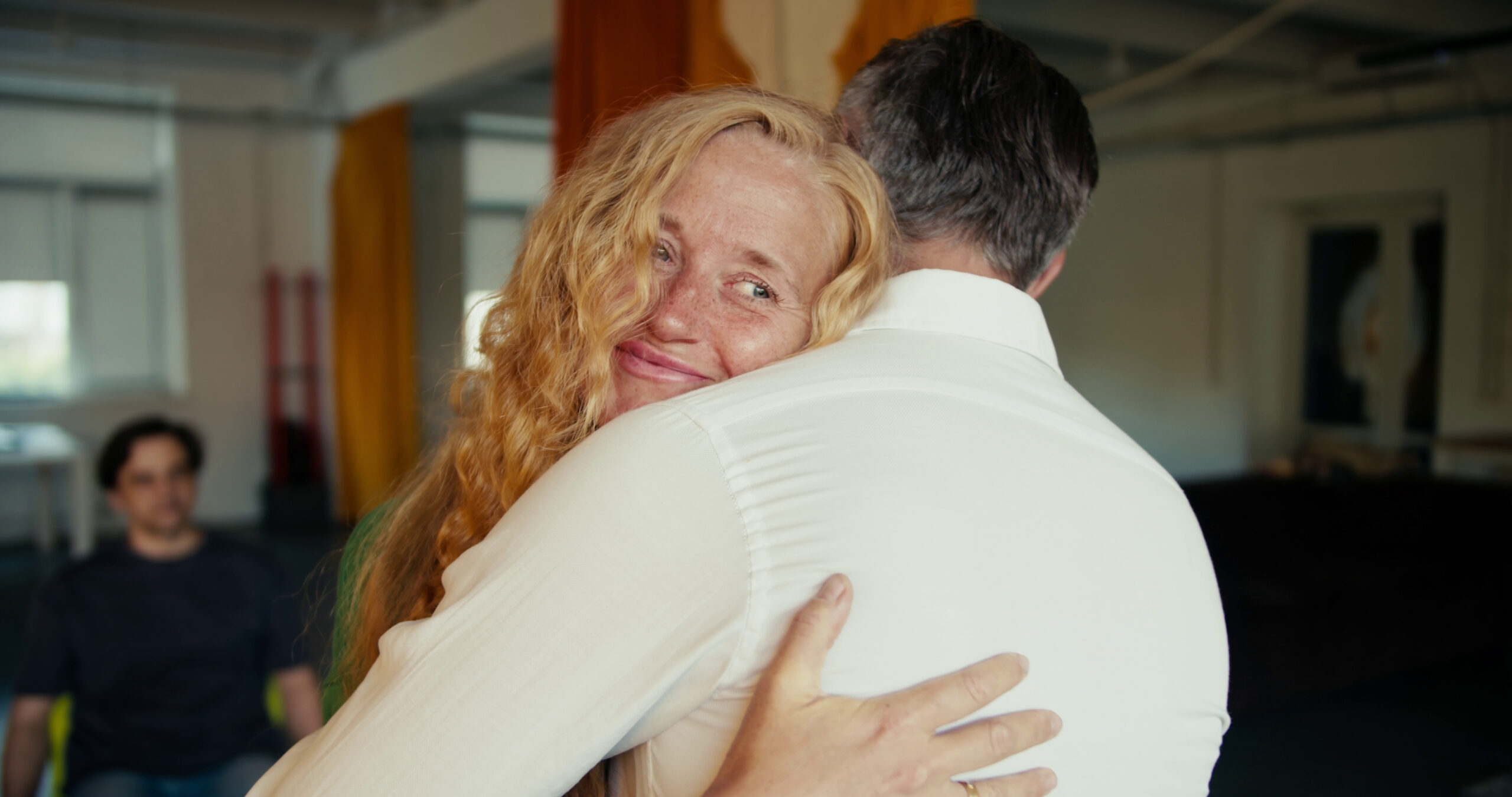 Blonde woman with curly hair hugs man with gray hair and a white button up