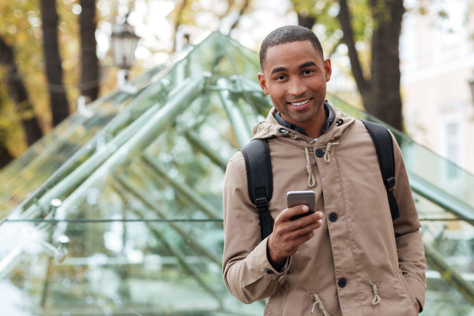 Cheerful young man holding phone and looking at camera