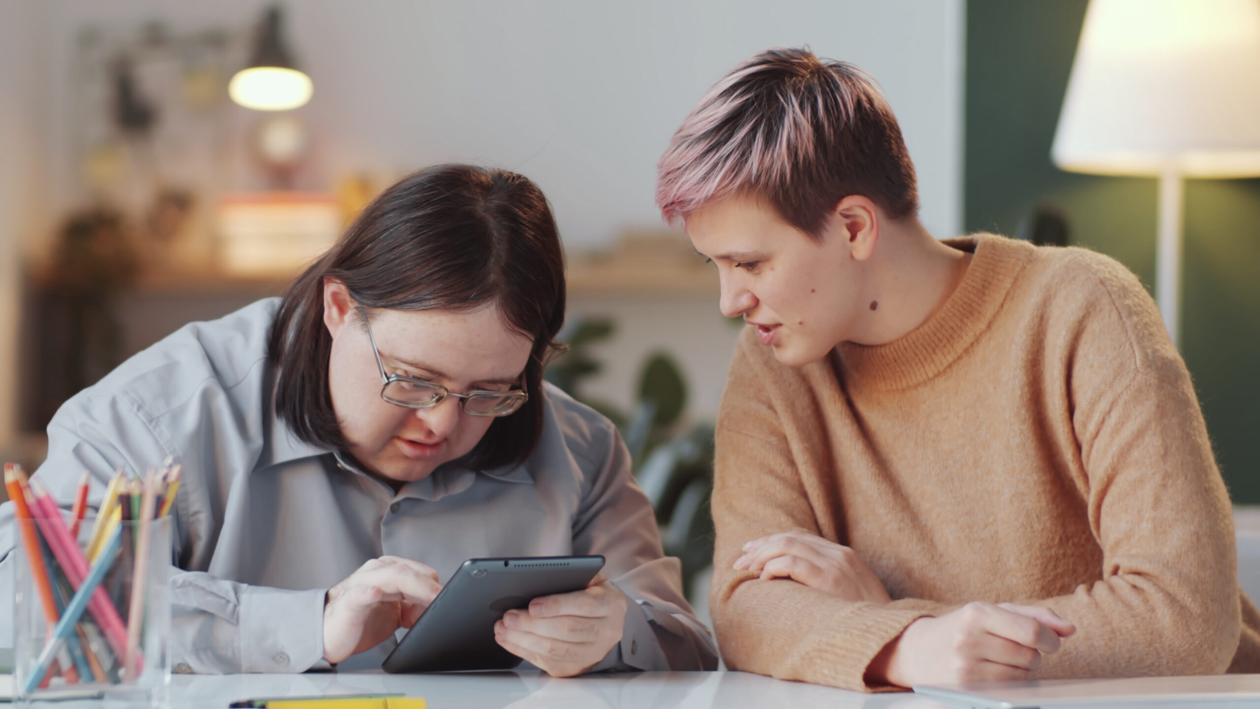 Female social worker sitting with an adult man with down syndrome at table looking at tablet