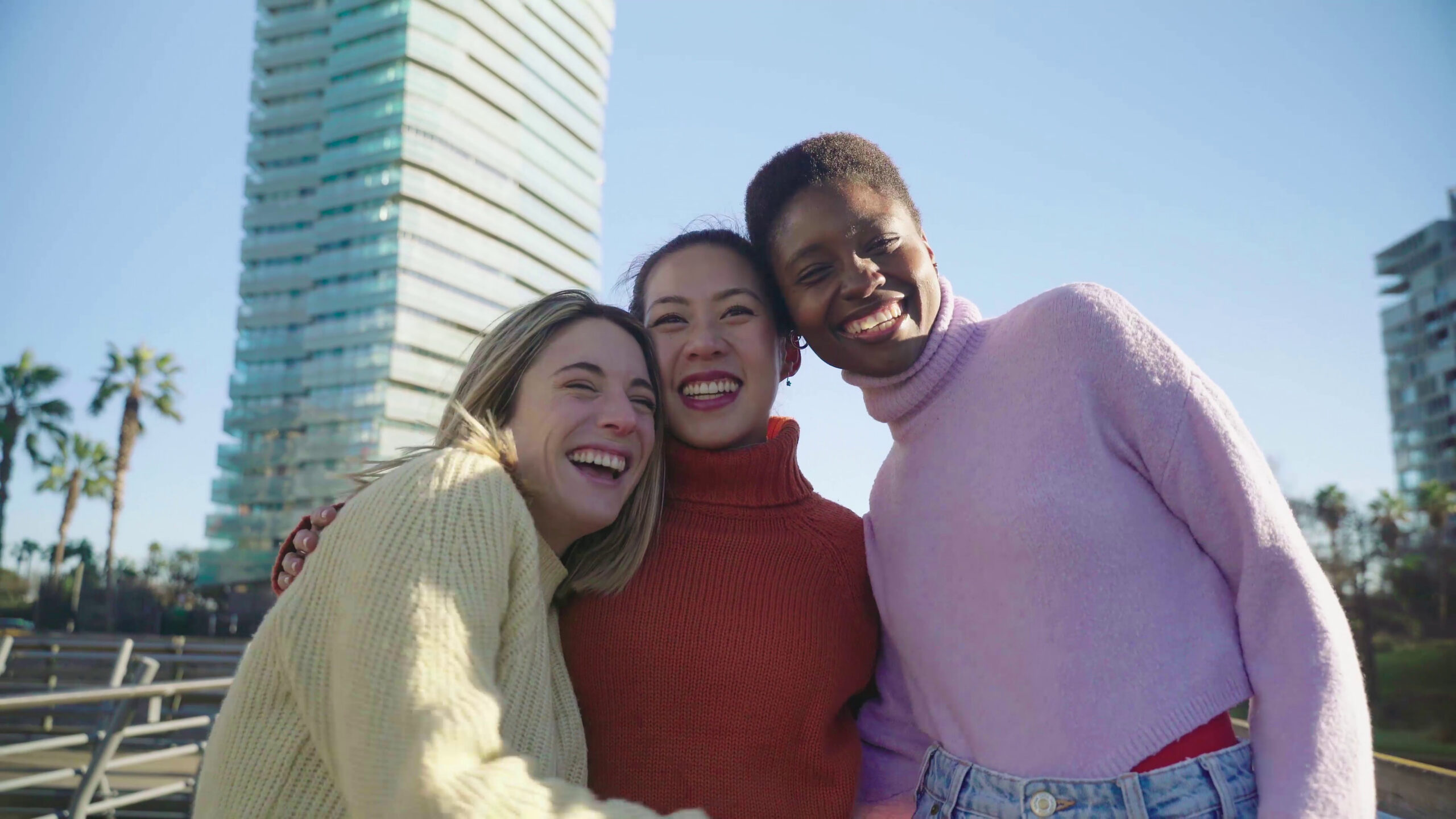 Three woman pose for a photo at the park all wearing sweaters and smiling/laughing