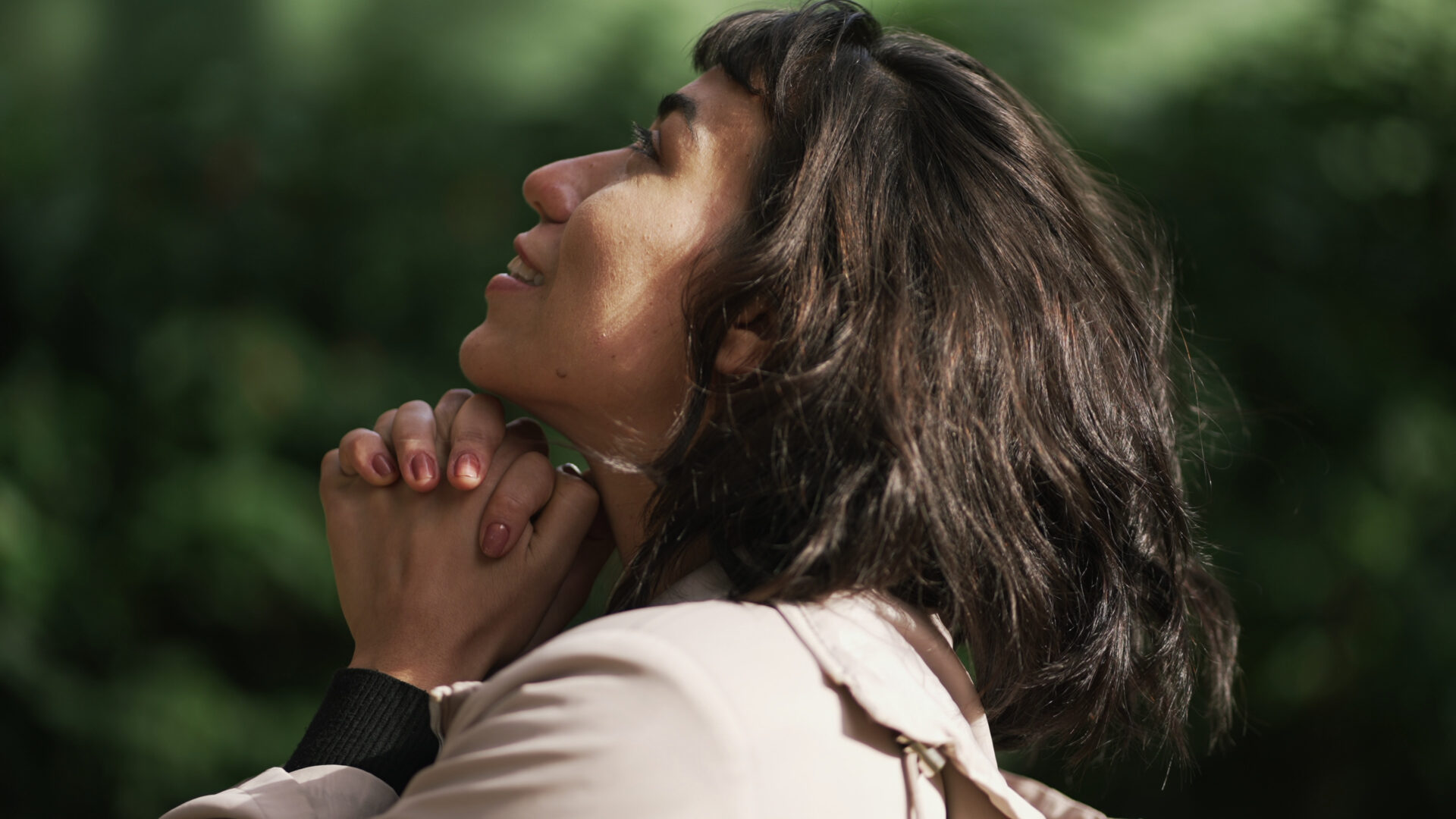 Hispanic woman with short hair and bands clutching hands and looking up at the sky